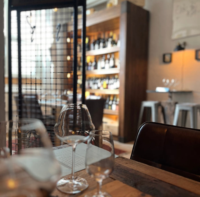 Vinglas på et træbord med vinreoler i baggrunden hos Sydhavnens Vinbar